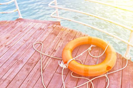 Orange lifebuoy with rope on a wooden pier near sea. Lifebuoy at the pier. Save lifebuoy and blue water.の写真素材