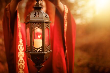 Woman in red holding a lantern with a candle. Hand lantern with a candle shines in the woods.の写真素材