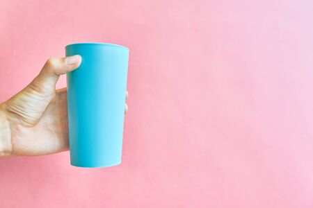 Colorful plastic cup. Paper cup in hands on bright pink background.の写真素材