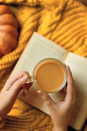 Mug of coffee, cozy knitted jacket, autumn, open book and pumpkin on wooden board. Autumn still life, vintage style. Flat lay.の写真素材