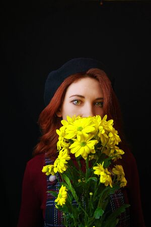 French redhead woman in plaid dress, Burgundy sweater and black beret holds and sniffs yellow chrysanthemumsの写真素材