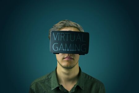 Young man in a shirt uses virtual reality glasses with the inscription virtual gaming on them in front of a dark green eden backgroundの写真素材