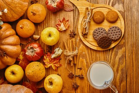 Cookies with milk on the table. Chocolate cookies and cinnamon on the wooden plate with a glass of milk and pumpkin with apple.の写真素材