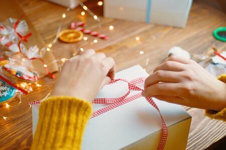Christmas composition with present box. The girl ties a red ribbon on the gift box.の写真素材