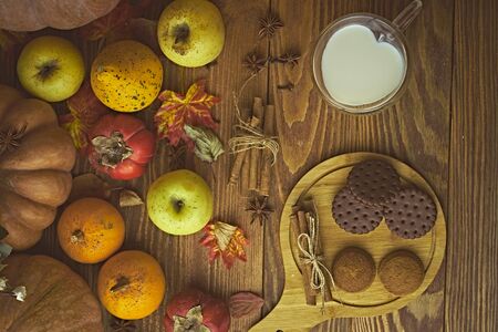 Cookies with milk on the table. Chocolate cookies and cinnamon on the wooden plate with a glass of milk and pumpkin with apple.の写真素材