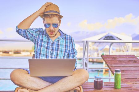 Concept of relaxing at sea. The man is working on time. The amazing face of the worker, in the computer. Shockedの写真素材
