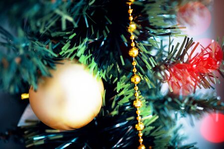 Yellow ball Christmas tree toy close up. Christmas ornament with lighted tree in background.の写真素材