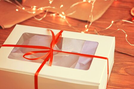 Christmas composition with present box. A Christmas gift box with a red ribbon stands on a wooden table.の写真素材