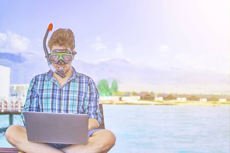 A man in an underwater mask, on vacation at sea, working at a computer.の写真素材