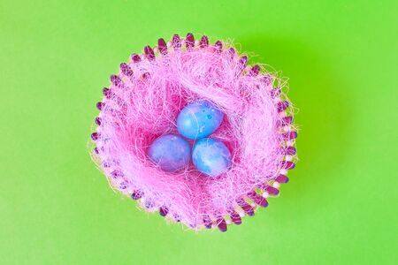 Three Easter eggs with space galactic pattern in a basket with a filler in the form of a pink nest on a green background. flat layの写真素材
