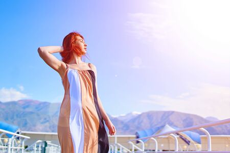 Woman in a dress stands on a pier on the beach by the ocean in a hotel against the background of mountains basking in the sunの写真素材