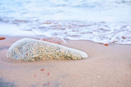 Sandy beach with waves from the sea. Rock in sand near the ocean.の写真素材