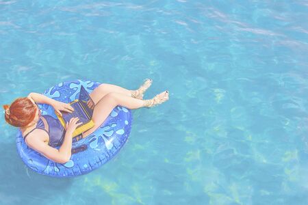 Beautiful young woman with on donuts and a desktop computer relaxing in the ocean.の写真素材