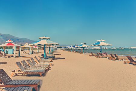 Sunbeds on the beach. A row of sun umbrellas with seats on the lake shore.の写真素材