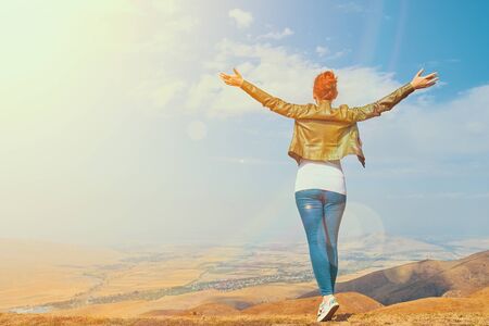 Woman in the mountain standing in the distance with her back to the camera and her arms outspread in celebration of a beautiful sunny summer day and freedom spread armsの写真素材