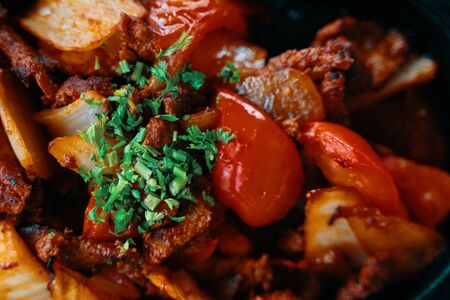 Fried food. Meat on a brazier with tomatoes and onions. View from above. Close up.の写真素材