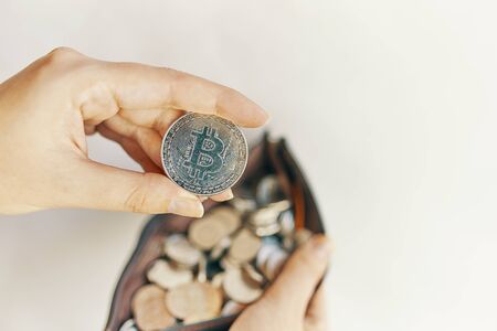 Woman holds Bitcoin coin. Silver bit-coin over many international money coins.