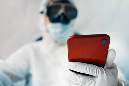 Virologist person protects himself from a global pandemic and holds a phone in his hands.