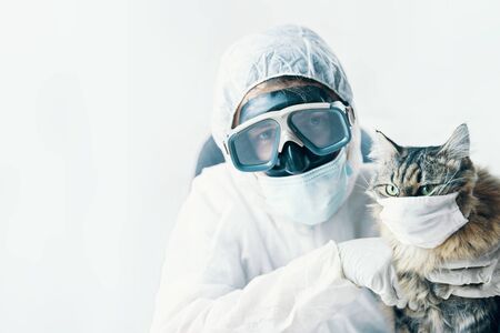 Man doctor in protective suit goggles with arms crossed and cat kitty is safe from coronavirus in medical protection mask. Pandemic worldの写真素材