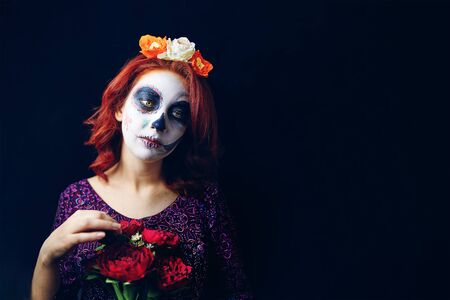 Sad red-haired woman with downcast eyes in day of the dead mask skull face art make-up on a black background. Halloween concept, copy spaceの写真素材