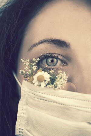 Macro eye portrait. Young attractive woman in floral face mask of flowers looking at camera in a studio in a mask during the coronavirus pandemic, new trend spring fashion.の写真素材
