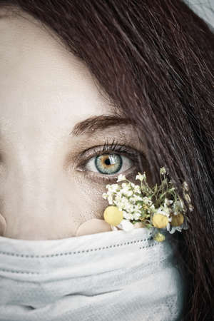 Macro eye portrait. Young attractive woman in floral face mask of flowers looking at camera in a studio in a mask during the coronavirus pandemic, new trend spring fashion.の写真素材