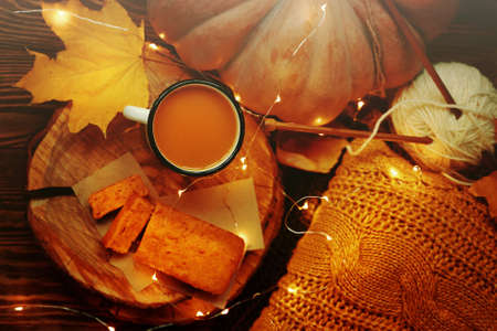 Top view of the autumn composition for postcards. Hot tea and pumpkin pie on a wooden tray. Ripe pumpkin and a warm knitted sweater with a ball of white yarn and needles on a dark wooden background.の写真素材