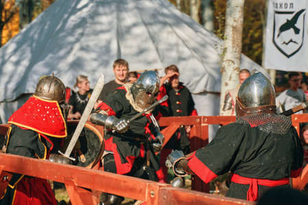 Medieval reenactment reconstruction of knightly battles during the festival of historical clubs. Three red-robed knights are fighting with swords. Bishkek, Kyrgyzstan - October 13, 2019.のeditorial素材