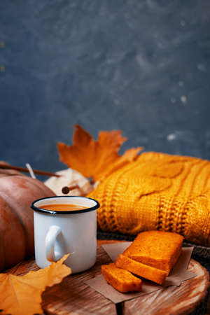 Fall composition with a blue background for Thanksgiving cards. Drink in a tin Cup and sweet freshly baked carrot cake on a wooden stand. Orange knitted sweater, pumpkin and yellow autumn leaves.の写真素材