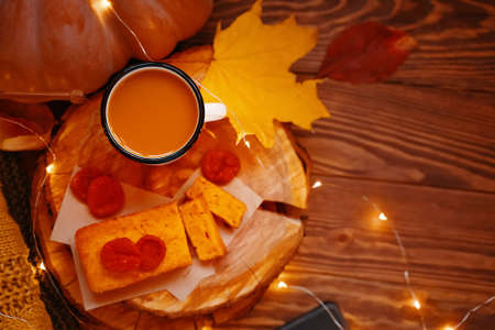 Top view of a festive composition with lights. Pie, pumpkin juice, dried apricots on a wooden tray. A knitted sweater, autumn leaves and a ripe pumpkin.の写真素材