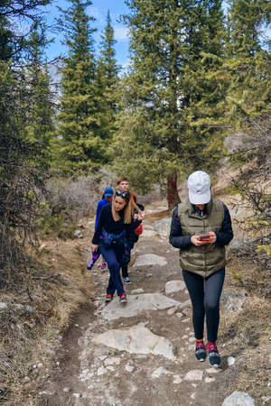 Travel along a beautiful mountain route. Front view of a group of people walking along a mountain path to the top. International mountain day. Bishkek, Kyrgyzstan - April 9, 2019.のeditorial素材