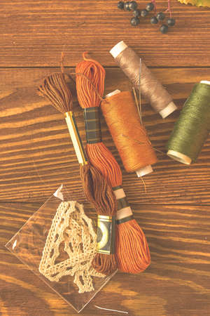 Floss yarn, laces, colored balls of thread and needles on a wooden background. Clothing designers desktop. Top view of the autumn composition. Hobbies, crafts, knitting and sewing.の写真素材