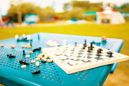 Chess and checkers are scattered on the table in the park. An intellectual game for developing strategy and tactics. Useful pastime on street. Resort entertainment. Chessboard and pieces on table.の写真素材