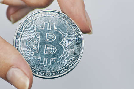 Woman holds Bitcoin coin. Silver coin with bit-coin symbol. Rise of cryptocurrency. New virtual money concept. Mining or blockchain technology.の写真素材