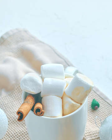 Cup of cocoa with marshmallows and cinnamon on the kitchen tablecloth. Hot chocolate in a white mug. The concept of Christmas and Thanksgiving. Christmas tree toy in the background.の写真素材