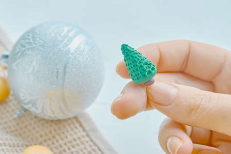Women holds Christmas toy in her hand. Tablecloth on the table. Christmas composition and fur-tree decorations.の写真素材