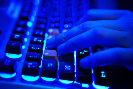 Multifunction keyboard with set of red button. WASD keys are used in many video games. Close-up on human hands on a neon lit keyboard, actively pushing buttons, playing games Online.の写真素材