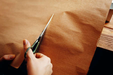 Hands cut sheet of craft paper with scissors. Wrapping for holiday gifts. Process of needlework.
