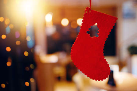 Christmas red felt stocking with carved Christmas tree. Concept of new year holidays. Christmas eve tradition. Sock on background of home environment. Holiday garlands and decorations.の写真素材