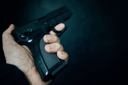 Criminal holding gun on black background. First person view of pistol. Firearm in mans hand. Defense or attack. Murderer or armed thief.の写真素材
