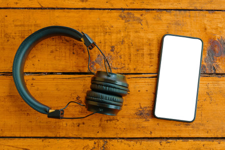 Top view of headphones and smartphone on wooden table. Mobile phone with blank white screen.  blogging. Copy space for text.の写真素材