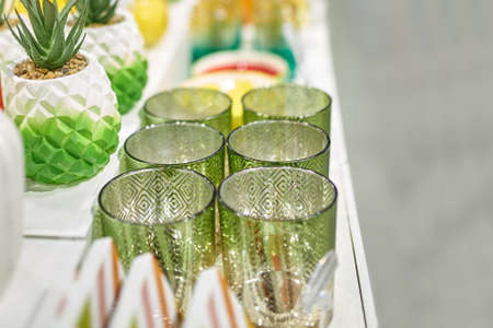 Shop window of home goods store. Patterned green glasses and planters with artificial succulent. White shelf with decorated dishes.の写真素材