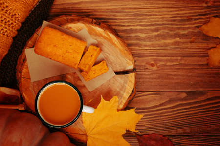 Top view of autumn composition with cup, a pumpkin, a pie and a sweater. Pumpkin juice and sweet freshly baked cake on a wooden tray. Warm orange knit sweater and yellow autumn fallen leaves nearby.の写真素材