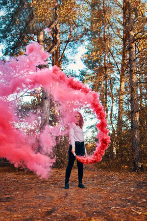 Smoke screen in the woods. Woman with smoke. Beautiful woman with pink smoke behind her in the forestの写真素材