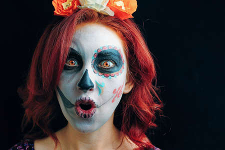 A young woman in day of the dead mask skull face art. Woman with Halloween skull make up over black background.の写真素材
