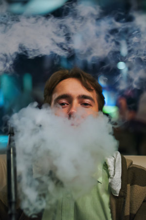 Portrait of a young man in the smoke. Man in restaurant smoking hookah. Person on sofa in cafe....