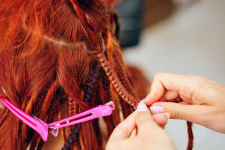 Hairdressers hands braid girls ginger dreadlocks. Beauty salon services. Hippie style hairstyle....
