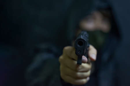 Man in hood and mask threatens with firearm. Revolver in persons hands. Murderer or armed thief....
