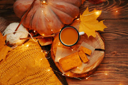 Flat lay of autumn composition for postcards. Hot coffee and pumpkin pie on a wooden tray. Ripe pumpkin and a warm knitted sweater with a ball of white yarn and needles on a dark wooden background.の写真素材