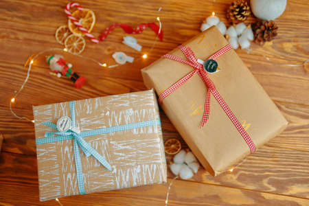 Wooden table with New years gifts and Christmas decor. Gift boxes in craft wrapping paper with white...